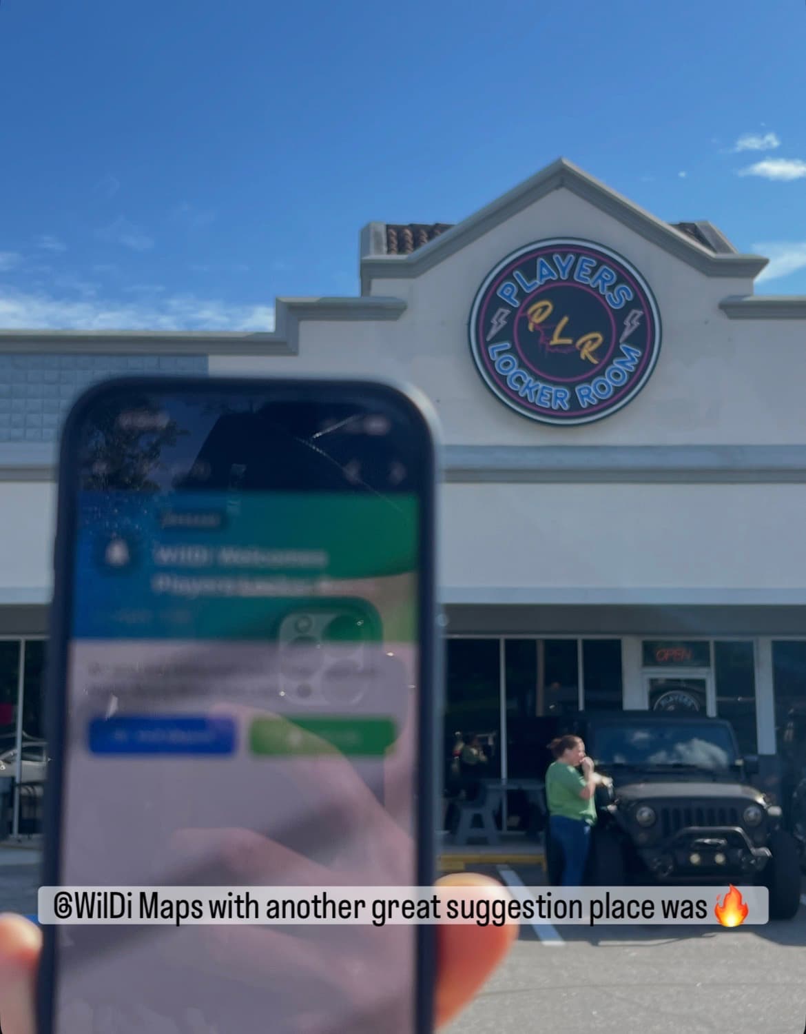 A customer holding their phone with the WilDi notification welcoming them to Players Locker Room, standing in the parking lot in front of the neon storefront sign.